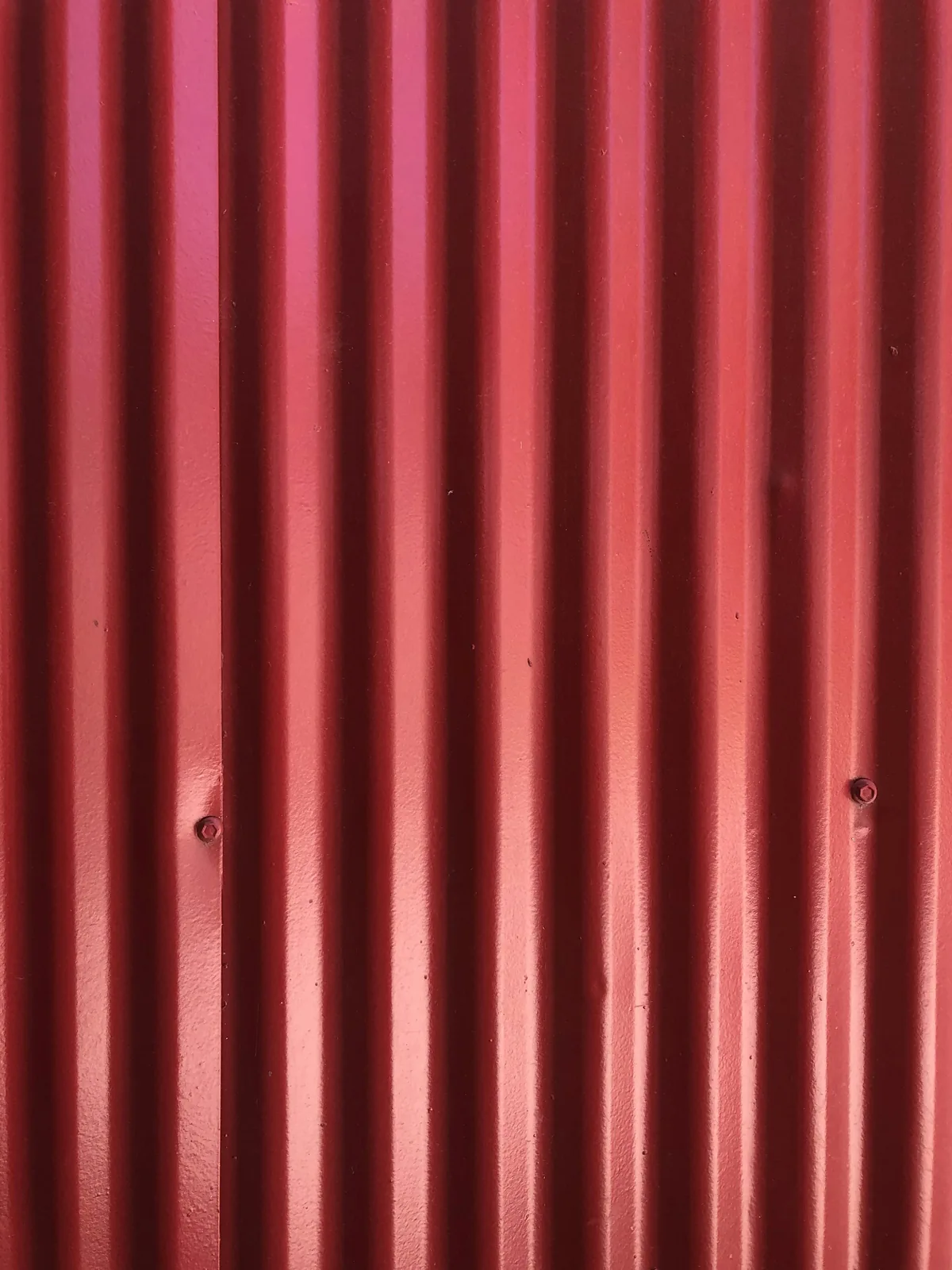 Close view of a red shipping container’s corrugated steel side, with vertical ribs, bolts and small surface marks.